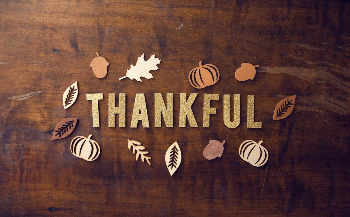 Text saying Thankful on a wooden background with cutout leaves and nuts around it.